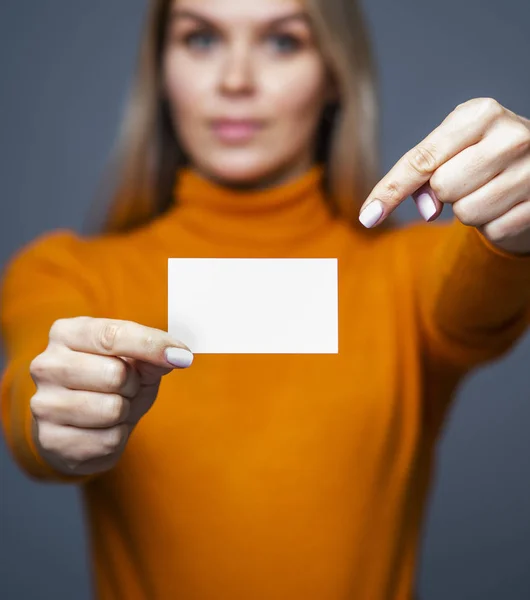 Incrível jovem segurando um mockup cartão de visita em branco e aponta com um dedo no cartão — Fotografia de Stock