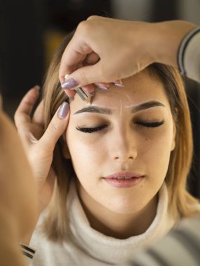 Gözleri kapalı, kaş şeklini düzeltme prosedürü olan genç bir kadın. Kalıcı mikropatinajdan önce yeni şeklin nasıl işaretleneceği konusunda sınıflar