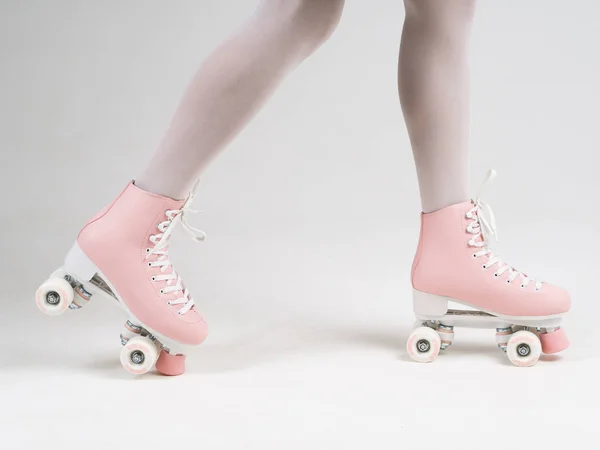 Side view female legs in white tights and pink four-wheeled roller skates shoes on a white background