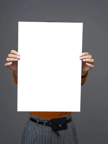 Menina adolescente elegante jovem com grande folha de papel em suas mãos sobre fundo cinza. Mockup vista frontal com espaço de cópia, sem rosto — Fotografia de Stock