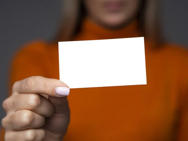 Uma jovem mulher em uma camisola laranja segura um cartão de visita ligeiramente inclinado com espaço de cópia — Fotografia de Stock