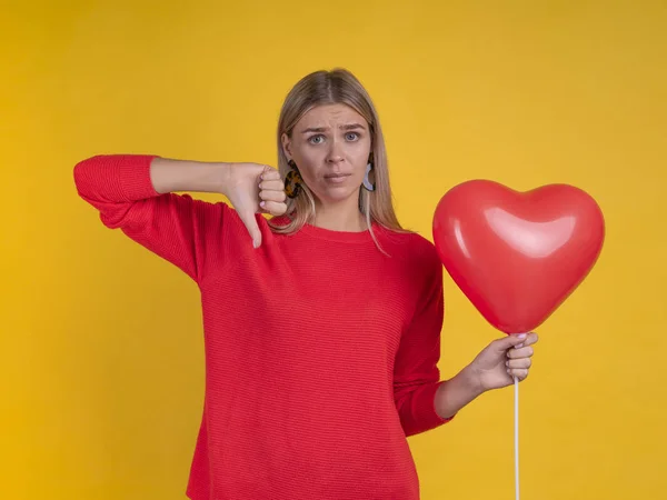 Sad Alone woman in red with heart balloon and thumb down gesture on Valentines Day. Dating concept