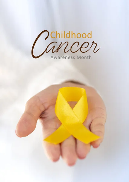 Vertical banner with text for Childhood Cancer Awareness. The female Hand holds yellow ribbon. Still life on white blurred background