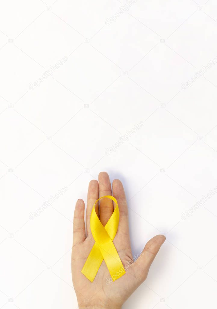 Vertical poster with hand holds yellow ribbon. Copy space for Childhood Cancer Awareness day banner
