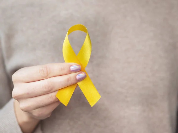 Acercamiento mujer sosteniendo una cinta de oro. La campaña de la cinta de oro lucha contra el cáncer infantil —  Fotos de Stock