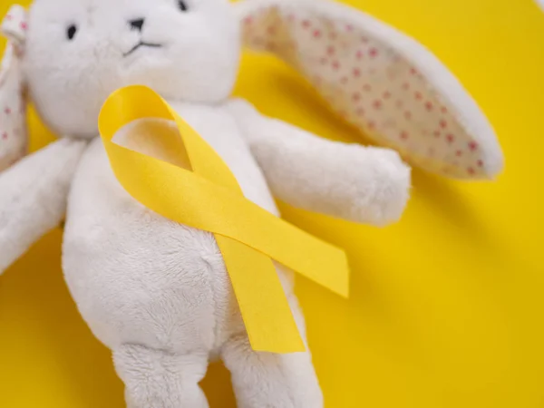 Febrero, 15 Liebre de peluche bodegón con una cinta de oro sobre fondo amarillo. Concepto del día de la concienciación sobre el cáncer infantil —  Fotos de Stock