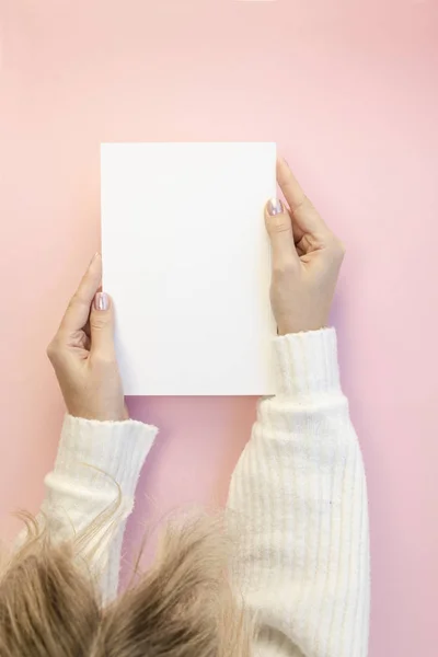 View from above Woman head and hands, holding a big white sheet or magazine with white copy space mockup. Flat lay on pink table