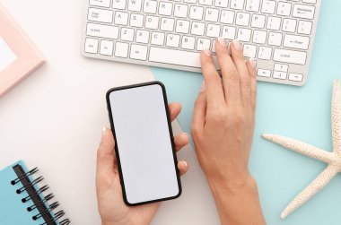 Büyük boş ekrana sahip siyah akıllı telefonu tutan ve gümüş klavyede metin yazan kadın el. Denizyıldızı ile üst görünüm seyahat mockup