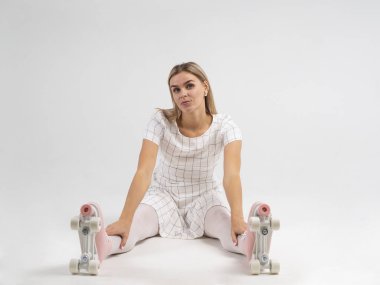 Beyaz zeminde oturan, eski model dört tekerli patenleriyle, sundress giymiş neşeli genç bir kadının portresi.