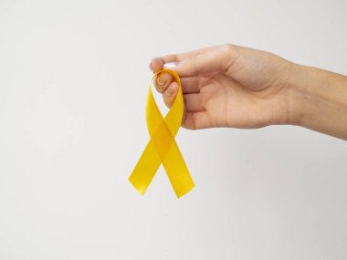Altın kurdele beyaz arka planda parmaklarda asılı. Uluslararası Çocukluk Kanser Günü konsepti