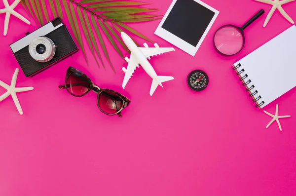 Płaska, żeńska rama wakacji na plaży z pustym spiralnym notesem, okularami przeciwsłonecznymi, aparatem fotograficznym i liściem palmy na różowym tle — Zdjęcie stockowe