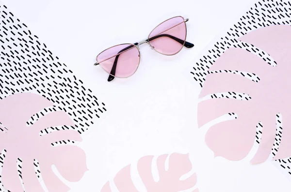 Moda minimale piatto laici occhiali da sole rosa e Papercraft monstera foglie di palma su uno sfondo bianco forme geometriche — Foto Stock