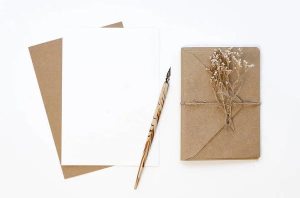 Flat lay Feminine workplace with wrapped with craft paper and twine gift card and empty paper card with ink pen and dry flowers. Mockup with copy space on a white table background — Stock Photo, Image