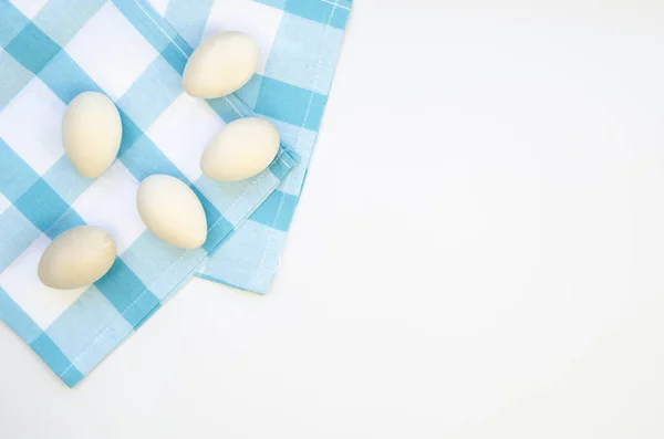 Ovos de madeira de frango artificial para decoração de Páscoa em um pano azul xadrez. Vista superior com espaço de cópia em um fundo branco — Fotografia de Stock