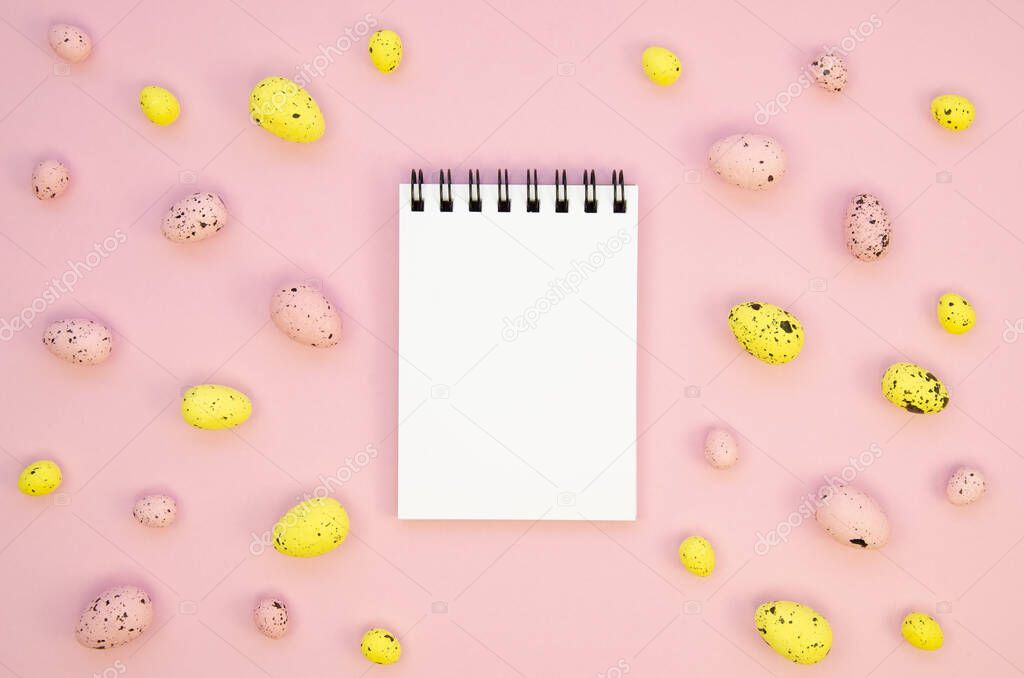 Blank spiral notebook bordered with quail Easter eggs on a pink table. Copy space for your text