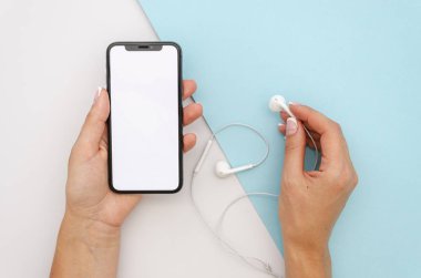 Kulaklık tutan kadınsı eller ve geometrik doku arka planında büyük boş ekran olan siyah akıllı telefon iPhone X.