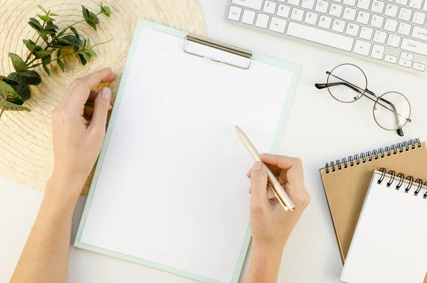 Papier a4 Klemmbrett-Attrappe. Weibliche Handschrift und Arbeit an einem weißen Schreibtisch mit Tastatur, Brille und Eukalyptus — Stockfoto