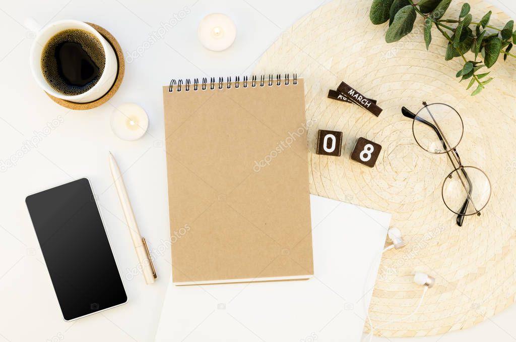 Top view 8 march wooden blocks calendar mockup with spiral notepad and blank screen smartphone. Office white desk with cup of coffee, glasses and candles