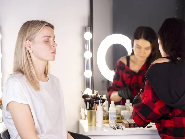 Beautiful blonde bride applying wedding make-up by a professional make-up artist in a studio — 图库照片