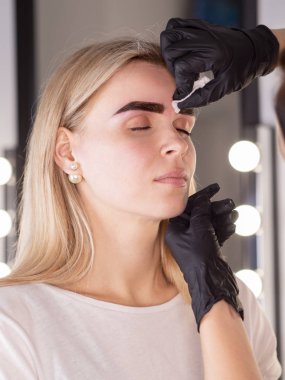 Güzellik uzmanı kaş çizgisini kozmetik pamukla kaş düzeltme üstüne kaş düzeltmesi yaparak siliyor.