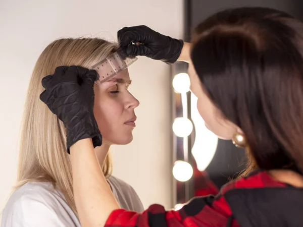 Professionell kosmetolog mäter med linjalen ett ögonbryn. Märker ny form. Permanent makeup koncept — Stockfoto