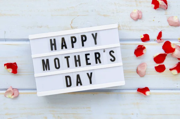 Flat lay Mothers Day lightbox rodeado de pétalos de rosa sobre tablones de madera de fondo — Foto de Stock