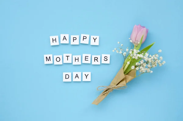 Señal de vista superior Happy Mothers Day hecha de cubos de madera blancos y ramo de flores de tulipán aislado sobre fondo azul — Foto de Stock