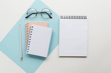 Sarmal defterleri, tahta kalemi ve beyaz arka planda gözlüğü olan düz bir çalışma masası. Metin için yer