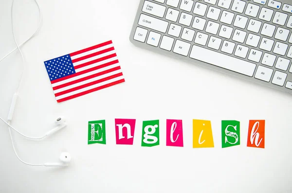 USA flag and word RUSSIAN on a white desktop with keyboard and earphones. Учить язык в домашних условиях — стоковое фото