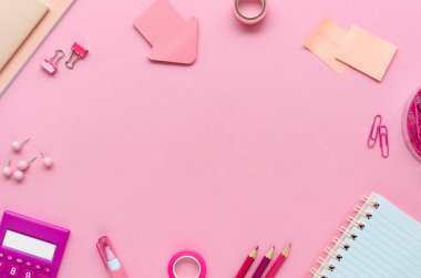 Pembe kağıtlı ofis masası, kalemler, kalemler ve pembe arka planda bir hesap makinesi. Boşluğu kopyalayan en küçük biçim üst görünüm çerçevesi