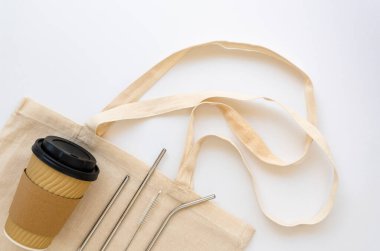 Çevre dostu yaşam tarzı seti. Yeniden kullanılabilir kağıt kahve fincanı, paslanmaz çelik pipet ve beyaz arka planda pamuk torbası. Düz yatıyordu