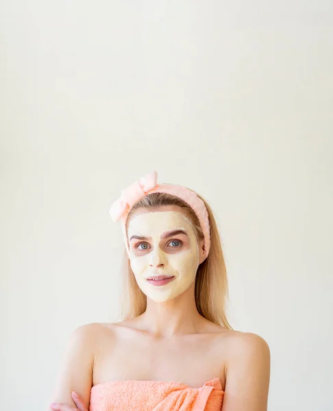 Beauty treatments at home. Vertical portrait of a young woman with a towel and a beauty mask on her face. Copy space for text