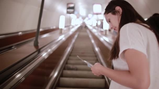 Pretty girl in subway. Brunette young woman in a white T-shirt on an escalator moving up. — Stock Video