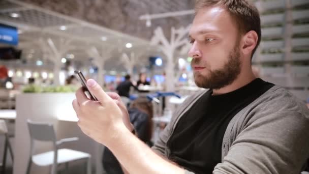 Un hombre guapo con barba usando su smartphone en un café. Tecnología moderna . — Vídeos de Stock