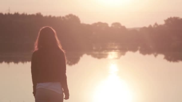 Menina lentamente levanta as mãos para cima desfrutando do nascer do sol no rio, em seguida, vira-se e olha para a câmera — Vídeo de Stock