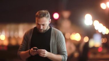 Yakışıklı adam sokakta yürüyor, telefonda konuşuyor, bağlantıyı keser ve gider. Şehir ışıkları bulanık. Modern teknoloji.