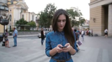 Sokakta yürürken bir kot elbise esmer güzel genç kadın. O onun smartphone kullanır. Yavaş mo, steadicam vurdu