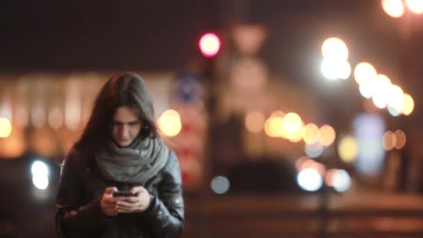 Mujer joven y bonita caminando por la calle, lentamente concentrándose. Una dama sonriente usando su smartphone. Tecnología moderna — Vídeo de stock