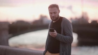 Yakışıklı adam akıllı telefon kullanan, kamera görünüyor, bir iskele üzerinde duruyor. İle a birden parlamak fotoğraf çekme. Modern teknoloji