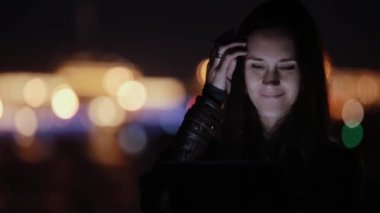 Geceleri gülümseyen genç ve güzel kadın tablet, kullanma. Renkli şehir ışıkları, arka plan bulanık. Modern teknoloji.