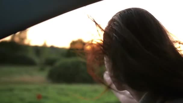 Femme heureuse sourit, aime voyager en voiture. Elle atteint son bras par la fenêtre d'une voiture. Le vent souffle les cheveux. Moteur lent — Video