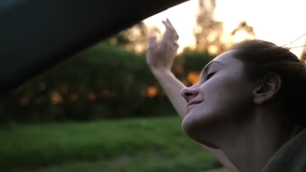 Mujer guapa en un coche, cerrando los ojos de felicidad, jugando con la mano en el aire. El sol se pone. El viento sopla pelo. Lento mo — Vídeos de Stock