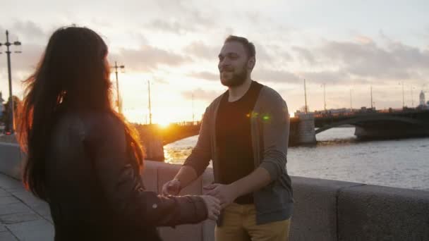 Щаслива пара обіймаються і закрученого навколо, як Сонце сідає в місті. Міст, річка, дорога, повільний МО — стокове відео