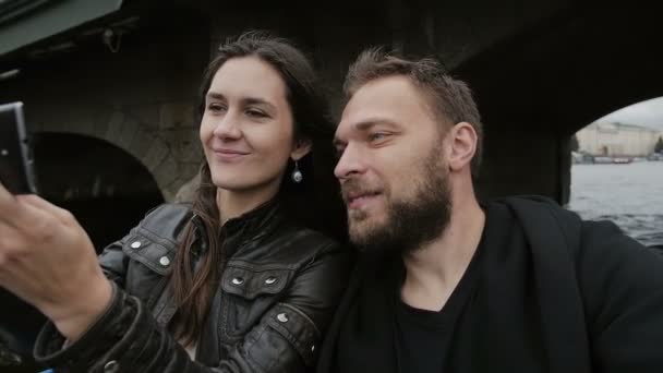 Felizes amantes sorrindo tirando selfie, usando smartphone. Passeio de barco em São Petersburgo, passando por uma ponte. Devagar. — Vídeo de Stock