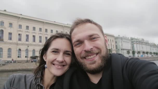 Synvinkel på ett lyckligt leende par som tar en selfie. Glada älskare i staden, man kysser sin kvinna, långsam mo — Stockvideo