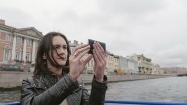 Çekim, smartphone kullanarak genç kadın bir nehir turu. Saç Rüzgar esiyor. St Petersburg şehir manzaralı. Yavaş mo