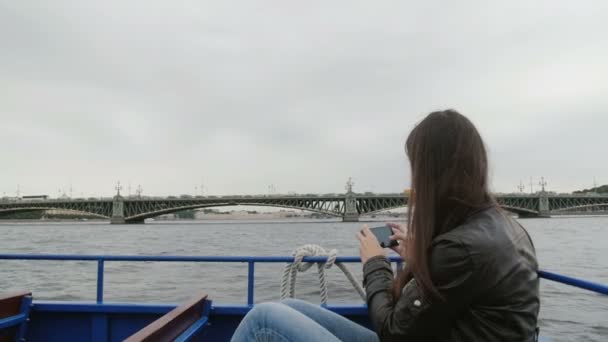 Dunkelhaarige Frau beim Fotografieren einer Brücke in St. Petersburg. Sie sitzt in einem Flussbus, der Wind bläst ihr die Haare, — Stockvideo