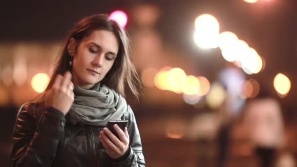 Bella giovane donna sorridente, utilizzando il suo smartphone di notte. Signora in strada con il freddo. Tecnologia moderna . — Video Stock