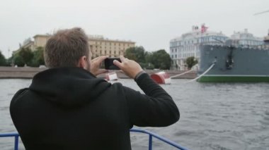 St Petersburg'da gezi. Adam akıllı telefon kullanıyorsa, bir teknede, yavaş mo tarafından geçen Cruiser Aurora fotoğraflarını çeker