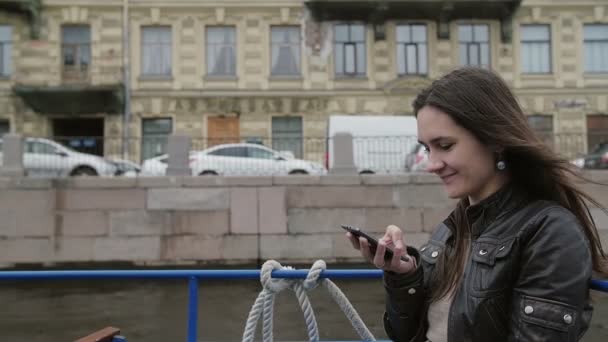 Glückliches brünettes Mädchen mit Smartphone, lächelnd. schöne Frau auf einer Bootstour, bewundernde Architektur, langsame mo — Stockvideo